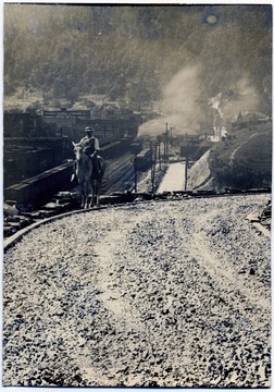 Man on horse (possibly Thoney Pietro) on edge of road under construction.  View overlooks railroad tracks and portion of town.