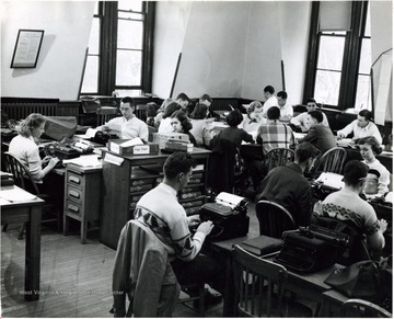 A room full of students working at typewriters in Journalism School.