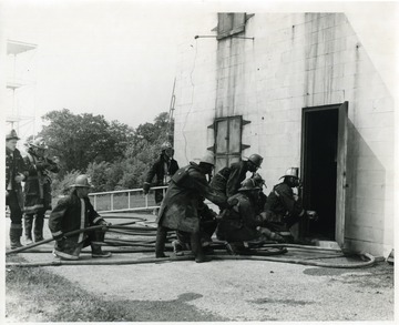 Fire School students using hoses and entering a building.