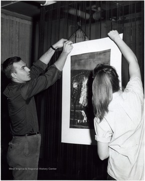 Joe Moss and a female student hanging a painting.
