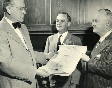 'H. T. Meek, news editor of the St. Louis Post-Dispatch; Professor George Simmons, president of the American Society  of Journalism School Administrators and Head of the department of Journalism, Tulane University, New Orleans; and Dr. P.I. Reed, chairman of the Committee of Awards of A.S.J.S.A and director of the School of Journalism of West Virginia University. President Simmons looks on as Dr. P. I. Reed presents to Mr. Meek a scroll containing a citation for the St. Louis Post-Dispatch in recognition of its objective criticism of governmental officialdom and the high standards of newspaper practice that it has maintained for nearly three-quarters of a century. The presentation took place at a luncheon in Pioneer Hall of the University of Minnesota on August 31, 1949, in connection with a joint meeting of A.S.J.S.A, A.A.T.J., and A.A.S.D.J.'