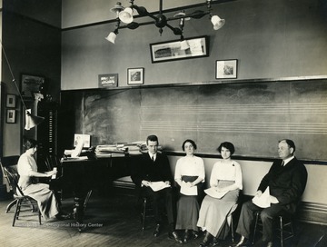 Three students and piano accompanist participate as performers in a musical group or as students in a music class; the rehearsal or class is being conducted in what appears to be a classroom in Woodburn Hall.
