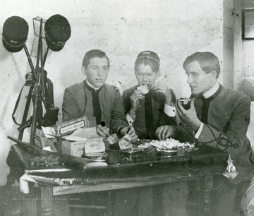 Three WVU Cadets enjoy a feast of tins filled with food and biscuits. Addison Dunlap Ellison, left; Charles Alexander Ellison, right; Center, unknown'.