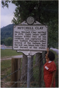 Historical marker regarding Mitchell Clay, with Joyce Balding Wood looking on. 'Here Mitchell Clay settled in 1775. Eight years later Indians killed two of his children and captured his son, Ezekiel.  Pursuers killed several of the Indians but the boy was taken into Ohio and burned at the stake.'  