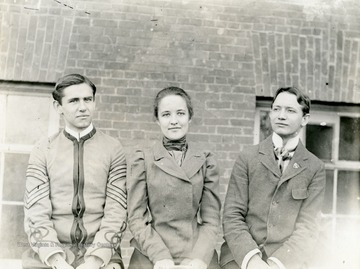 A female student, Carrie Dent, flanked by two male students, one in a cadet uniform.  Carrie Louise Dent, WVU Class of 1899, was one of the first 20 woment to graduate from the University and the daughter of Marmaduke Dent, Class of 1870, WVU's first graduate.  She married Professor Robert Armstrong, Class of 1886, in 1901.  