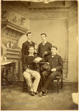 Group of four unidentified students, posed before a fireplace. Inscribed on the front; "a hard crowd".