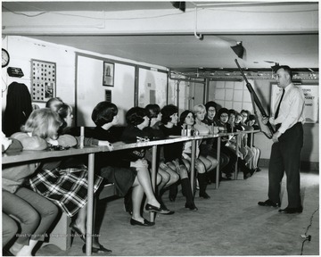 Man holding rifle while female students watch.