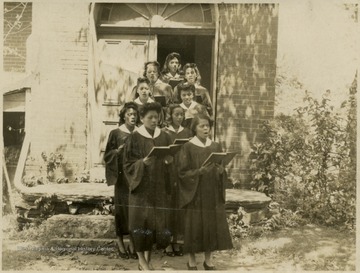 Group of African-American, female students, dressed in choir robes exit a church singing.