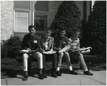 Four young men sitting outside on a bench studying in front of the Agriculture Building.