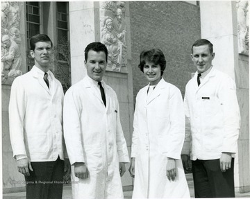 One woman and three men pose in medical jackets outside Medical Center. The name tag on the gentleman on the far right reads: Mr. M.D. Adams.