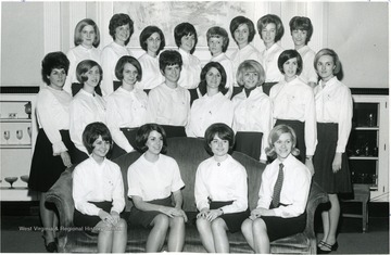 Group portrait of female members of WVU Panhellenic Council in Elizabeth Moore Hall with their backs against the fireplace; members dress uniformly in white top and dark bottom.  