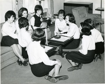 WVU female members of Panhellenic organization gather informally.  They dress uniformly with white long sleeved top with a dark skirt and low flats.  