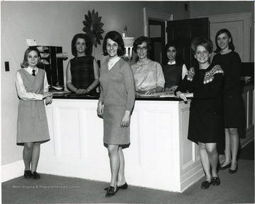 Members of Activities Board of Associated Women Students gather around a reception desk near the entrance of Elizabeth Moore Hall; 2nd from left Sudie Horman, 3rd from left Judy Skunda, 4th from left Becky Clise and 5th from left Carolyn Peluso.