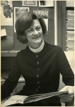 Portrait of Associate Professor of English Aileen Shafer, shown seated with a publication in her hands in an office.