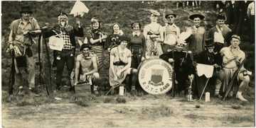 Members of WVU ROTC Band pose for a group photo as winners of Old Clothes Parade on a hillside.  A few sponsors are present among cadets.  Most of the male cadets wear costumes improvised from kitchen items to musical instruments etc.