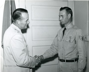An active duty Air Force Staff sergeant shakes hands with an Officer in an R.O.T.C. office.The sergeant is being awarded an Army Commendation Medal.