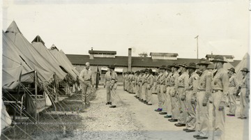 R.O.T.C. cadets in summer training camp; two officers stand between rows of cadet and a row of pitched tent, one cadet is stepped forward. 