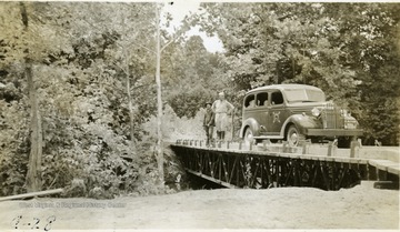 A cadet and an officer stand by a car on a bridge.