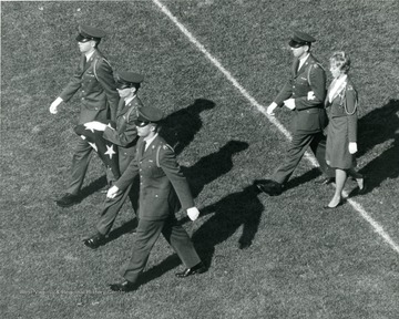 Cadets carrying a folded flag walk on the football field.