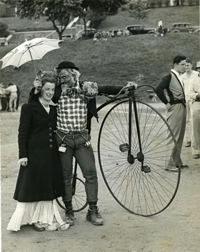 A cadet hugs a sponsor dressed in costume next to a classic highwheel bicycle.