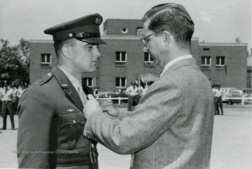 A cadet is receiving a badge from a man in civilian clothes.