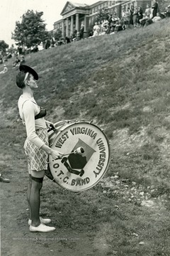 A band member dressed in a female attire strikes a drum for audience.