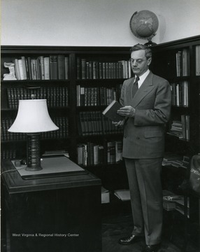 President Irvin Stewart in an office in front of bookshelves with a book in his hand.