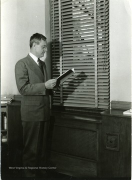 President Irvin Stewart stands by a window with a book in his hands.