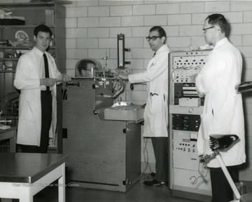 Subject (Donnelly) is in a machine; Russakoff operates the machine, while Lapp monitors a recorder.  Kaplan stands farther left.