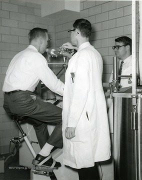 A subject is on a test machine, while two researchers monitor the progress.