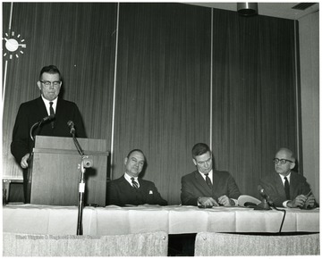 'Dean of the WVU Graduate School John Ludlum (left) is shown introducing main speaker Everett Walters, Vice-President for Academic Affairs of Boston University (second from left), at the Dec. 6, 1967 seminar on the Future of Graduate Education at WVU.  Panelists seated are Paul Selby, Dean of the College of Law (second from right), and Leo Fishman, Professor of Economics and Finance (right).'