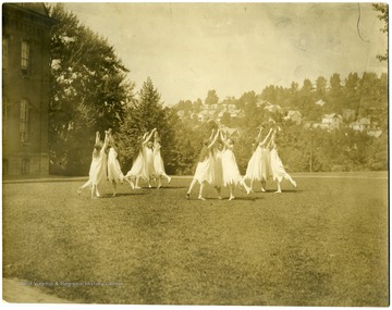 A group of female students in a flowing costume dance barefoot on Woodburn Circle.
