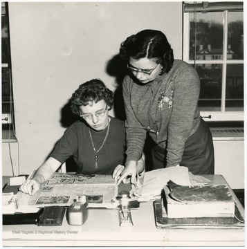 Joan Ellis and Martha Jones examine a newspaper article.