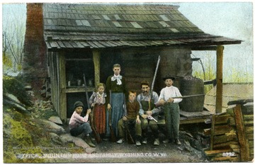 Picture postcard of a typical wooden mountain home and family all holding rifles.