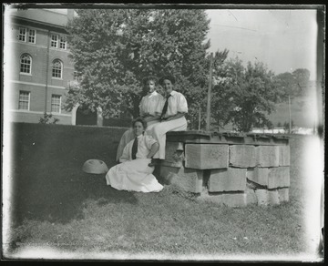 Three female students pose at well, Science Hall (Chitwood Hall) is in the background. Pre 1926.