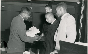 Student in a gown shakes a man's hand.