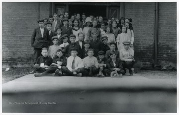 A group of young students gather for a group portrait in front of entrance.