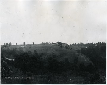 A view of state farm. Fences run across the hill and farm structures, barns and silos are visible in the distance.