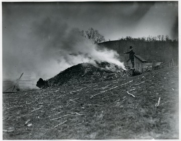 A man watches over a pile of burning material.