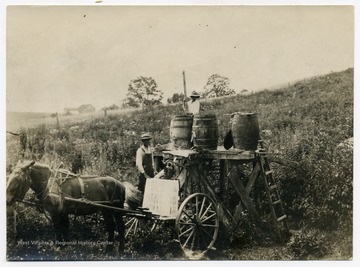 Farm workers in a field with a horse drawn cart with barrels.
