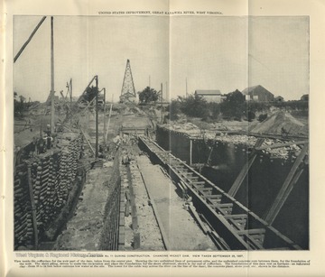 'United States Improvement, Great Kanawha River, West Virginia.  View inside the cofferdam for the weir part of the dam, taken from the center pier. Showing the two unfinished lines of permanent cribs, and the unfinished concrete core between them, for the foundation of the weir. The sheer piling, driven to make the excavation and place the foundations for the shore abutment, shown in far end of cofferdam. The foundations of this dam rest on hardpan - an indurated clay - from 18 to 24 feet below extreme low water at the site. The tower for the cable way across the river (on the line of the dam), concrete plant, stone yard, etc., shown in the distance."