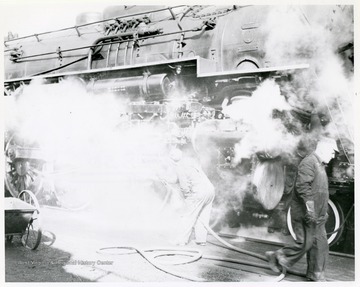 Image from the collection of the Chesapeake and Ohio Historical Society. 'CSPR--285: Workman steam cleansing running gear of C. &amp; O. Hudson (L-2) #300 at Hinton, W. Va. engine terminal.'