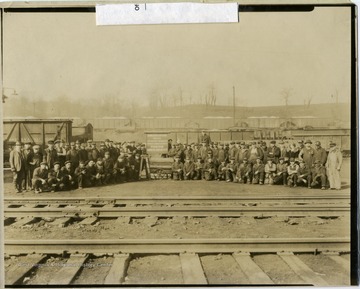 The workers at the Shire Oaks car shop in Washington, Pa. pose behind the rails: on the sign and a cart in the middle of the group has a few safety slogans for workers written.