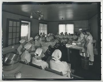 A group of ladies sit in a class, learning how to can food. 