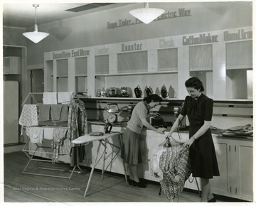 Females demonstrate electric appliances in a show room.