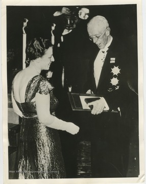 'Stockholm, Sweden...in a brilliant ceremony in the flower-decked great hall of the Stockholm Concert House, Pearl Buck, American writer, is shown receiving from King Gustav V of Sweden the 1938 Nobel Prize in Literature.  Nine members of the Swedish Royal Family, the entire diplomatic corps and outstanding representatives of Sweden's Cultural and Scientific bodies looked on as the 80-year-old Monarch handed Mrs. Buck a parchment certificate bound in tooled leather, the Nobel medal and a check for an amount equal in American money to about [unreadable].'