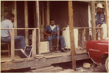 Fred Carper playing the Guitar as Thomas Brown and neighbor listen.