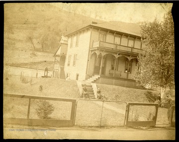 'Second home of M. H. Dent family - facing Barrett St. in Grafton, W. Va. - directly behind and above first home.  Judge Dent & Herbert on steps - Mrs. Dent & Carrie under tree.  Probably taken around 1890-95.  He later built a large brick house on Washington Street uphill from Post Office.  It is still standing.'