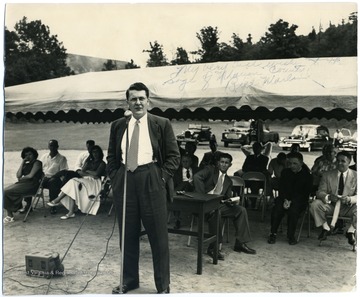 Group seated behind Marland under a canopy. 