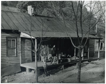 House has a metal roof; young boy standing next to porch.  Laundry hanging and wash tubs on porch.